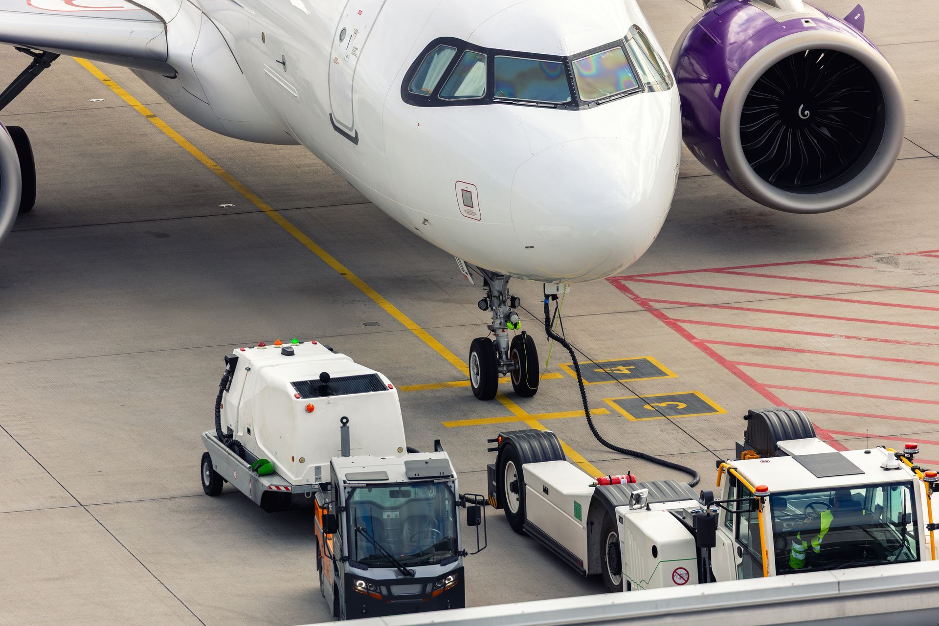 Airplane being serviced at an airport: fuel truck, baggage handlers, and tow trucks near aircraft.