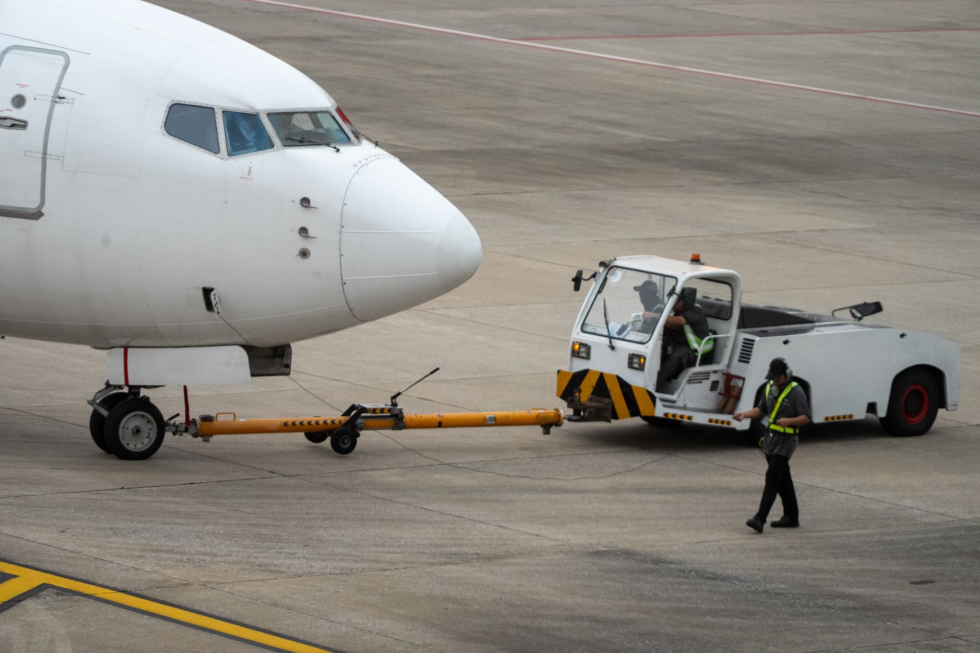 Airplane being towed by a tug on an airport tarmac; a worker stands nearby.