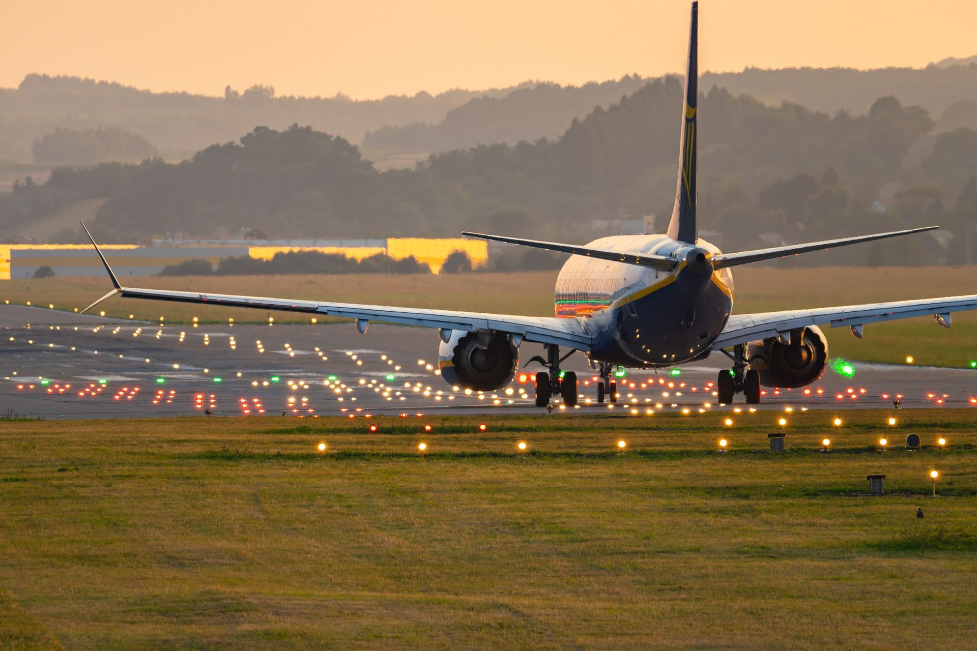 Aircraft taxiing on runway with illuminated lights at airport during early evening hours.