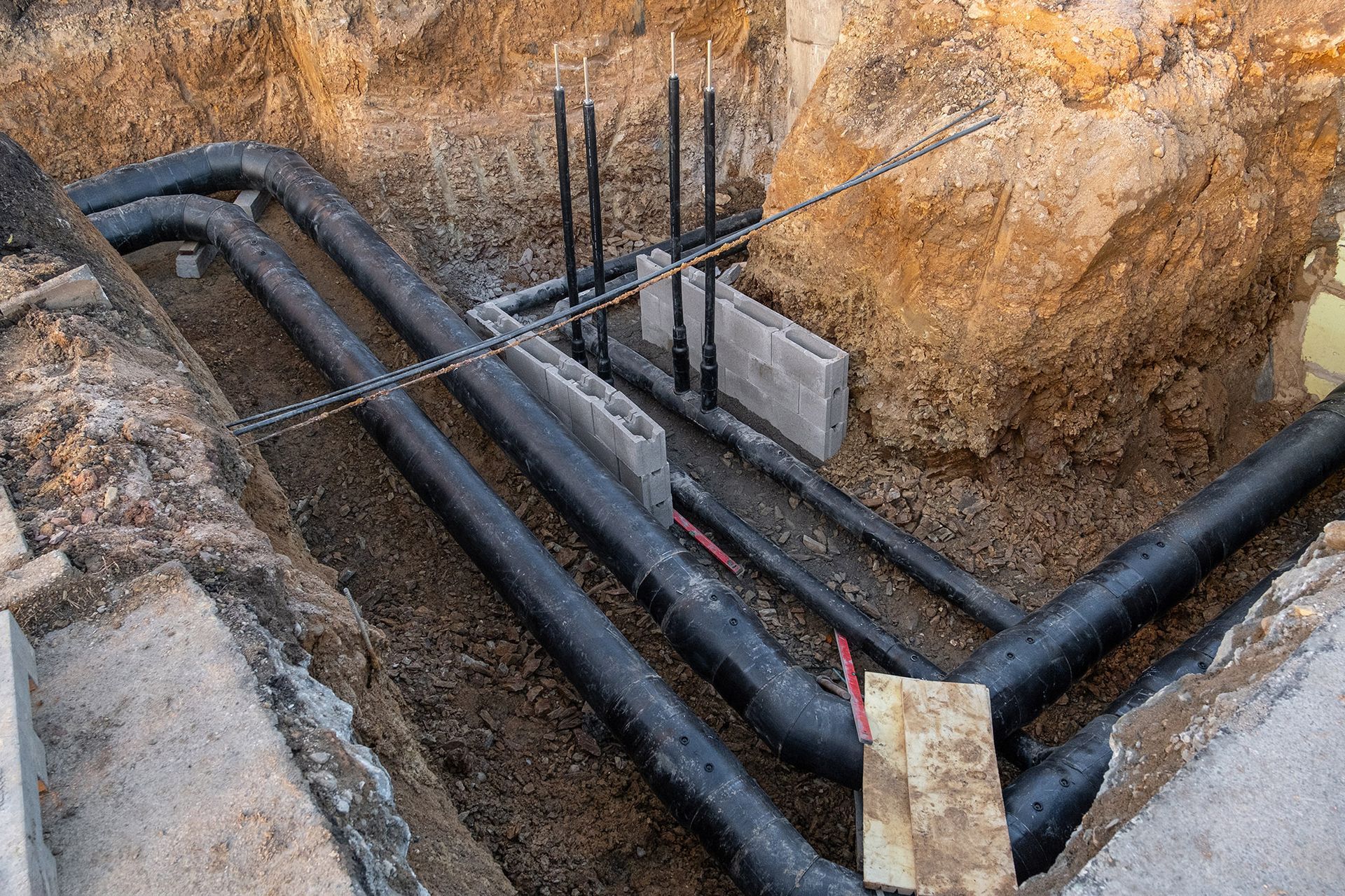 Black pipes and rebar in an excavated trench, possibly for utilities or infrastructure.
