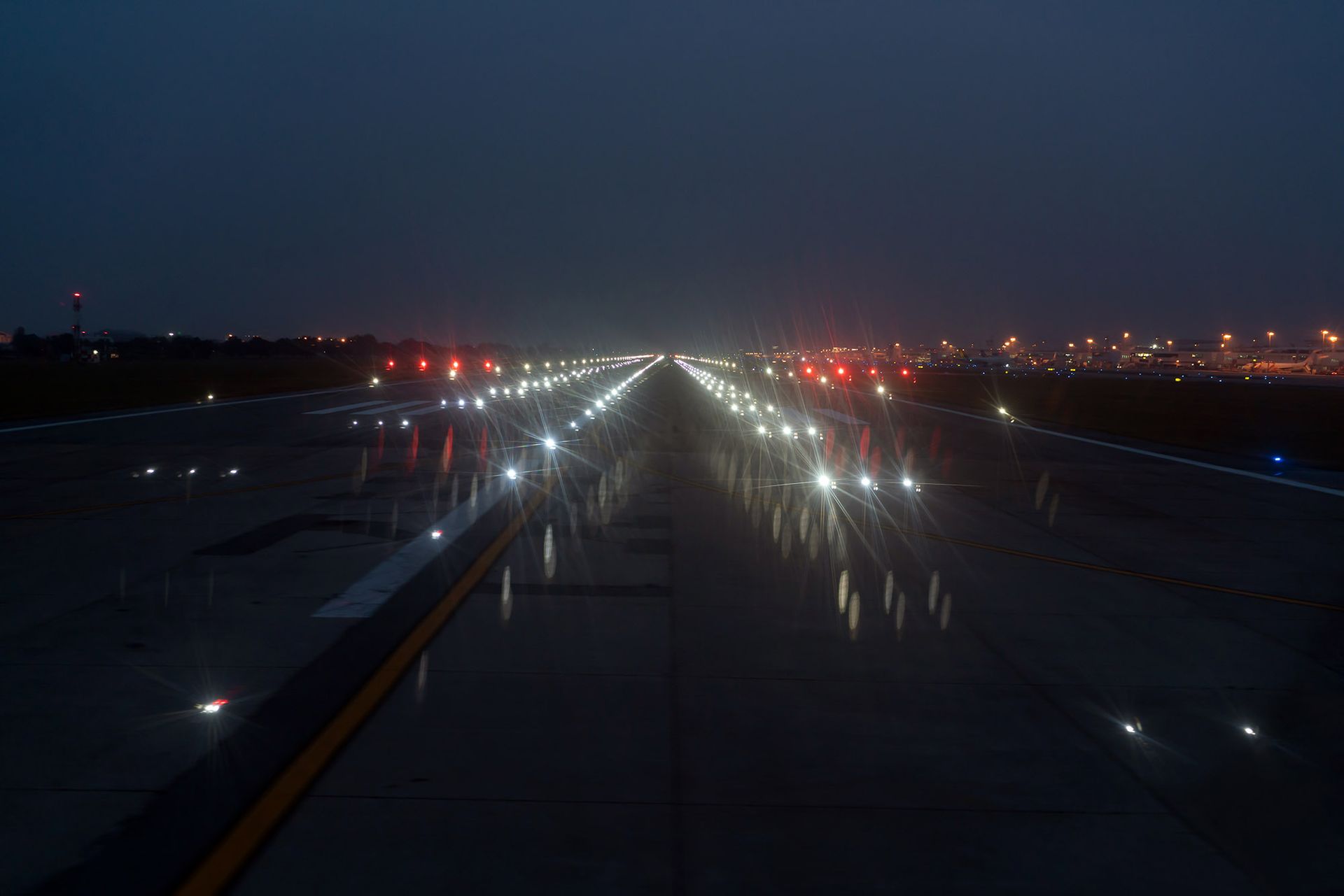 Nighttime airport runway lit with bright lights stretching into the distance.