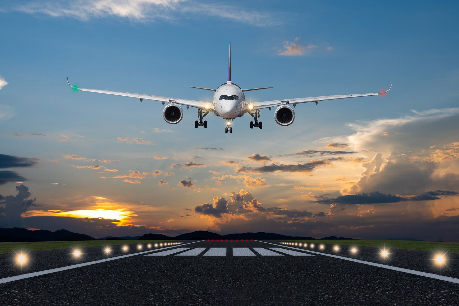 Airplane landing on a runway at sunset; orange and blue sky, lit runway lights.