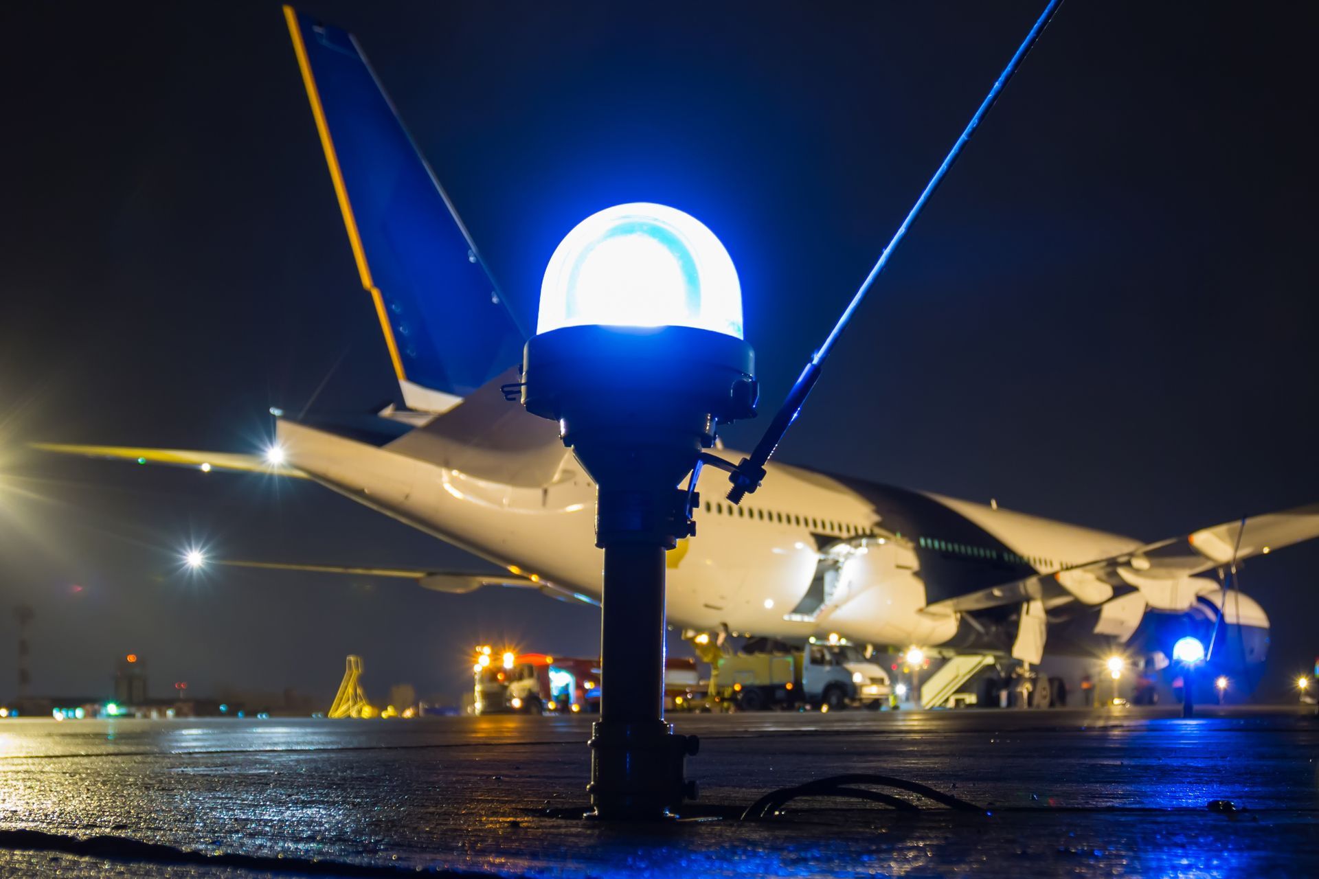 A close-up of a taxiway side row light in the foreground of a large passenger aircraft at night.