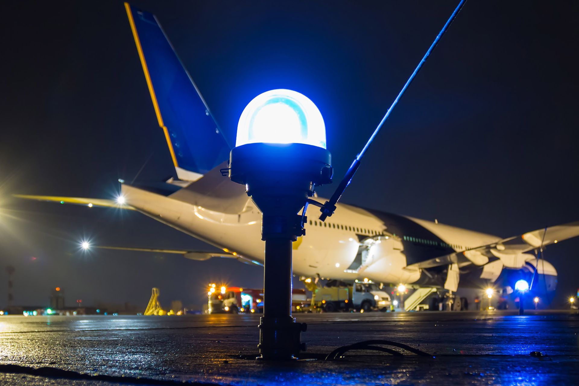 Blue airport taxiway light, airplane in background, night.