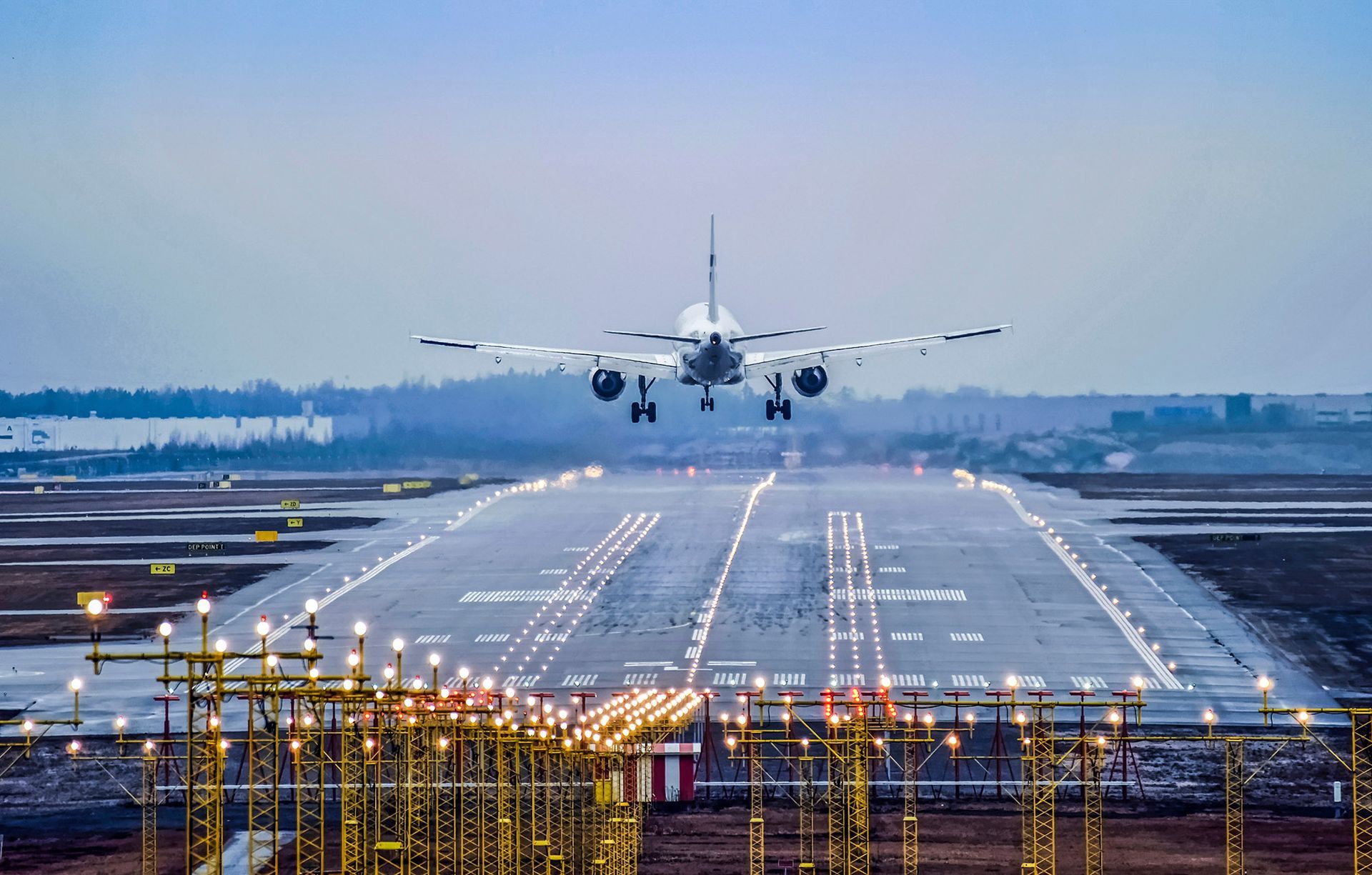 Airplane about to land on a lit runway at dusk.