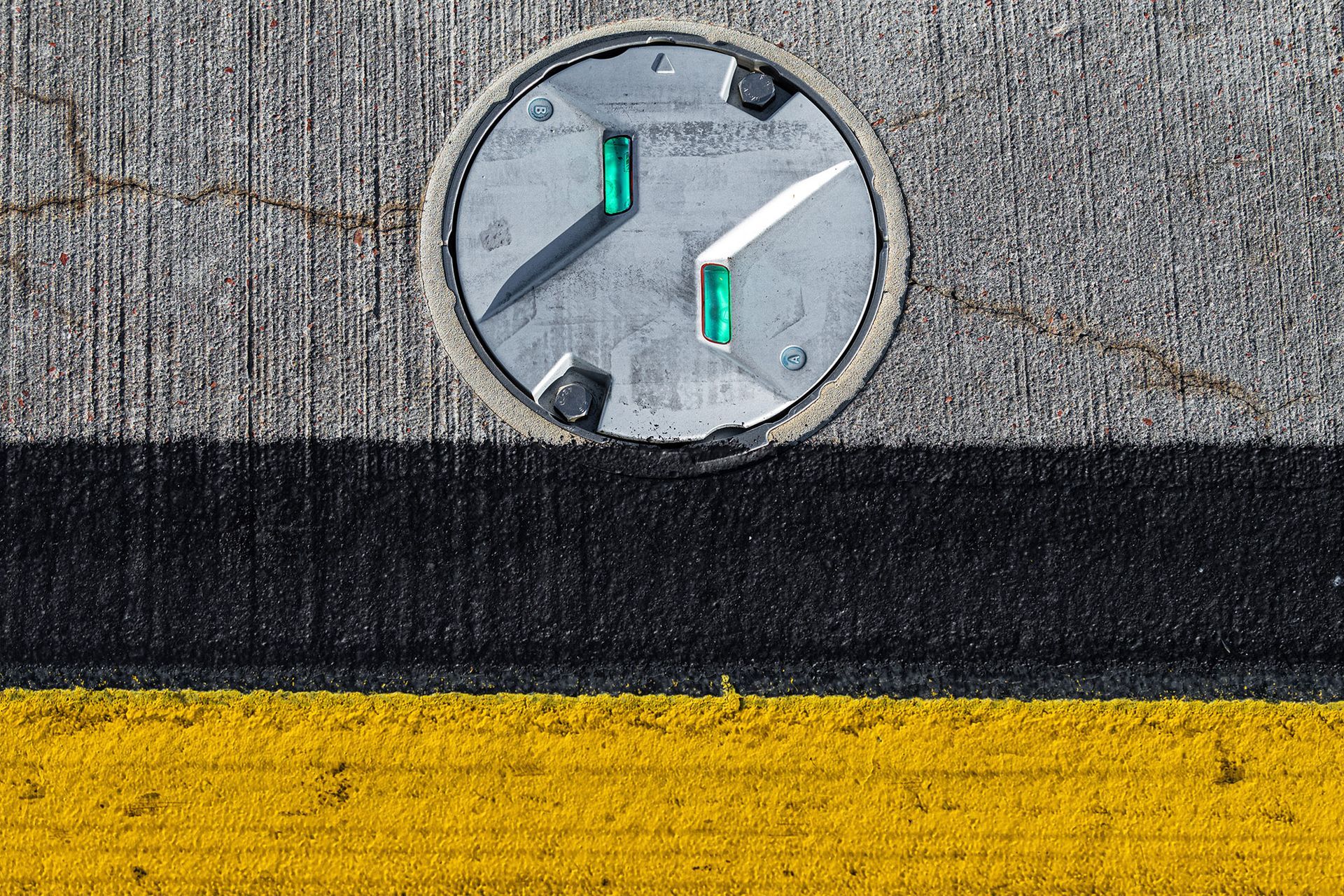 Circular metal electrical outlet embedded in concrete, with black and yellow road markings below.