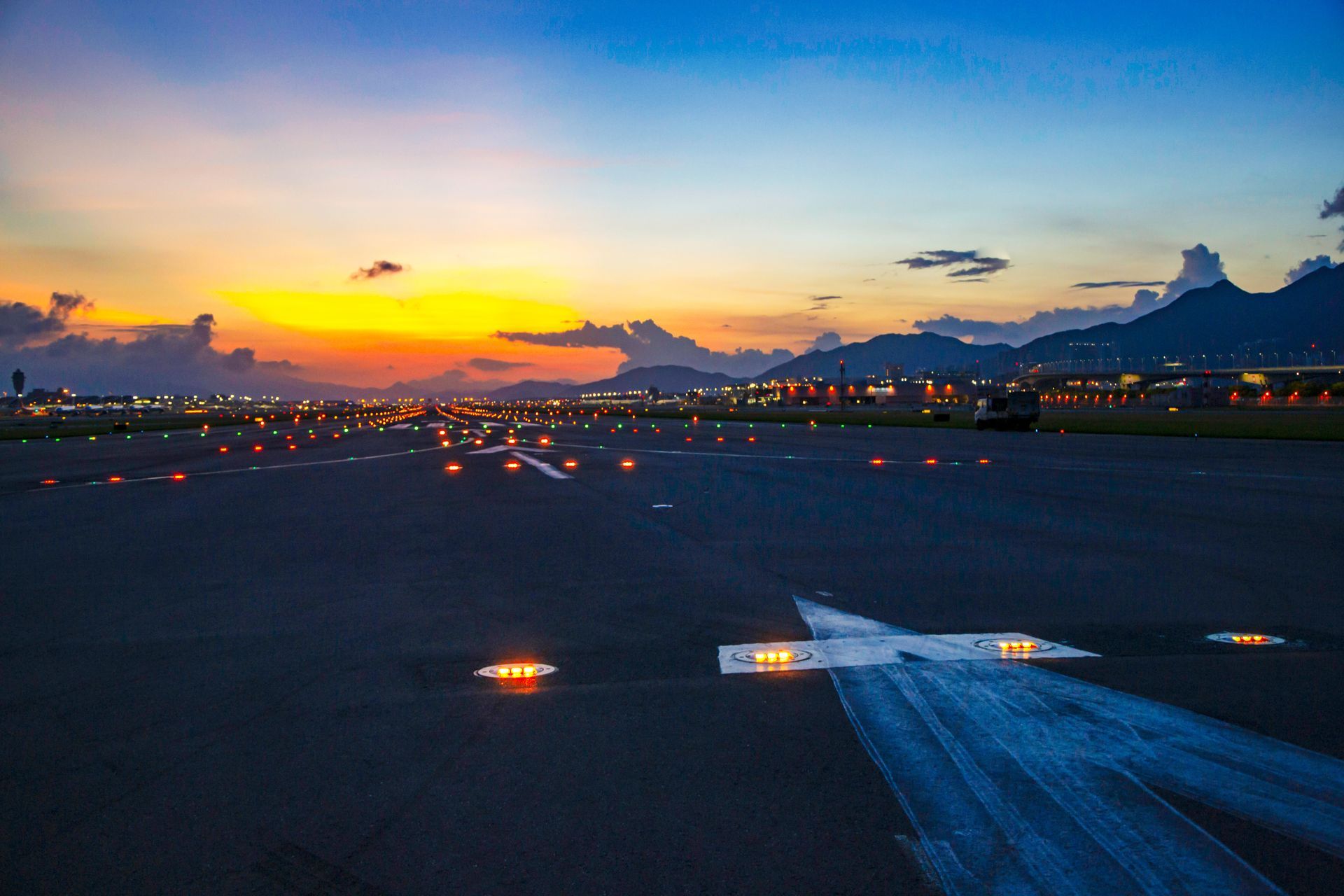 Airport runway at dusk with lit runway markers and colorful sunset.