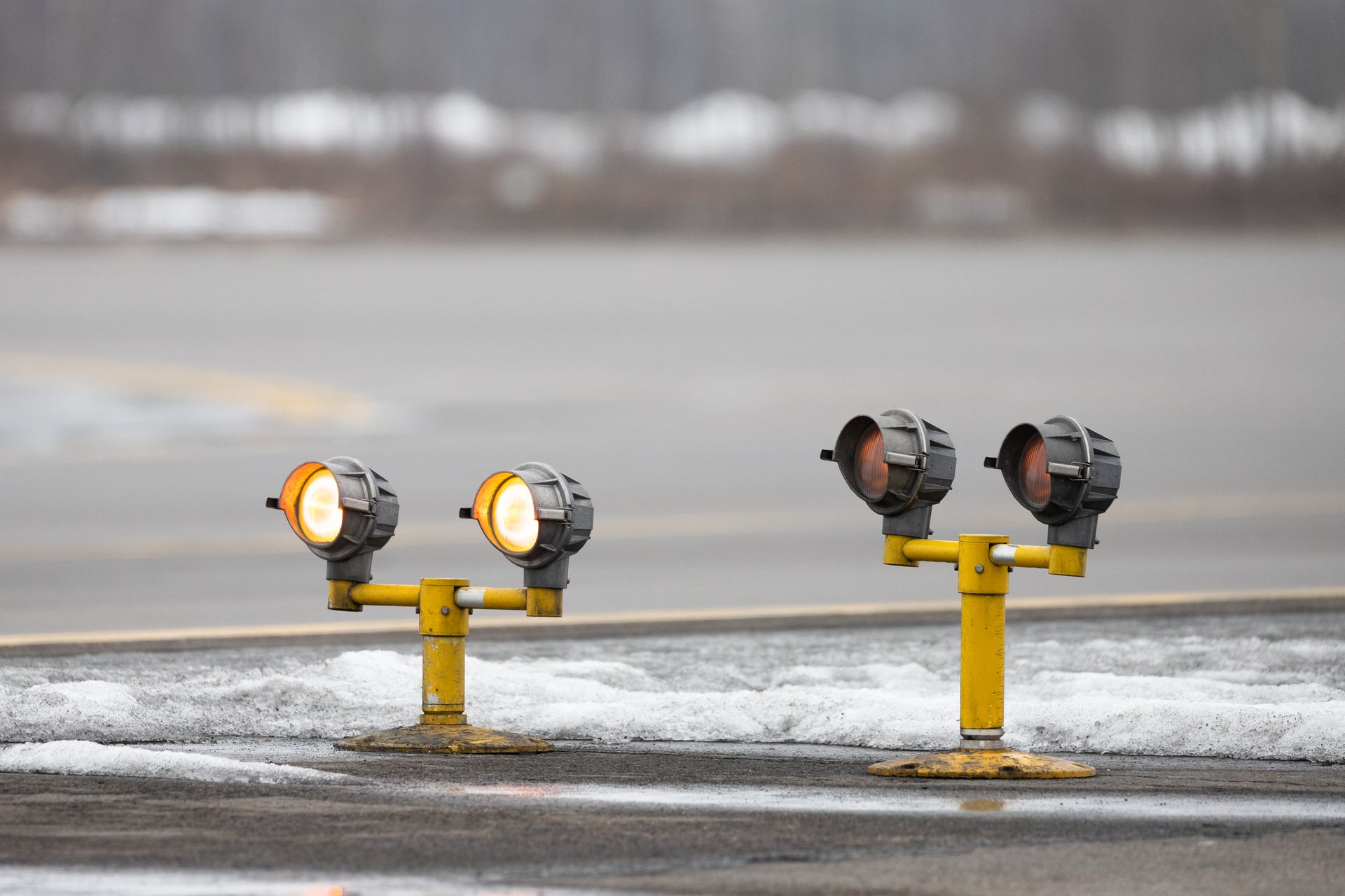 Yellow runway lights on gray asphalt with a snowy, blurred background.