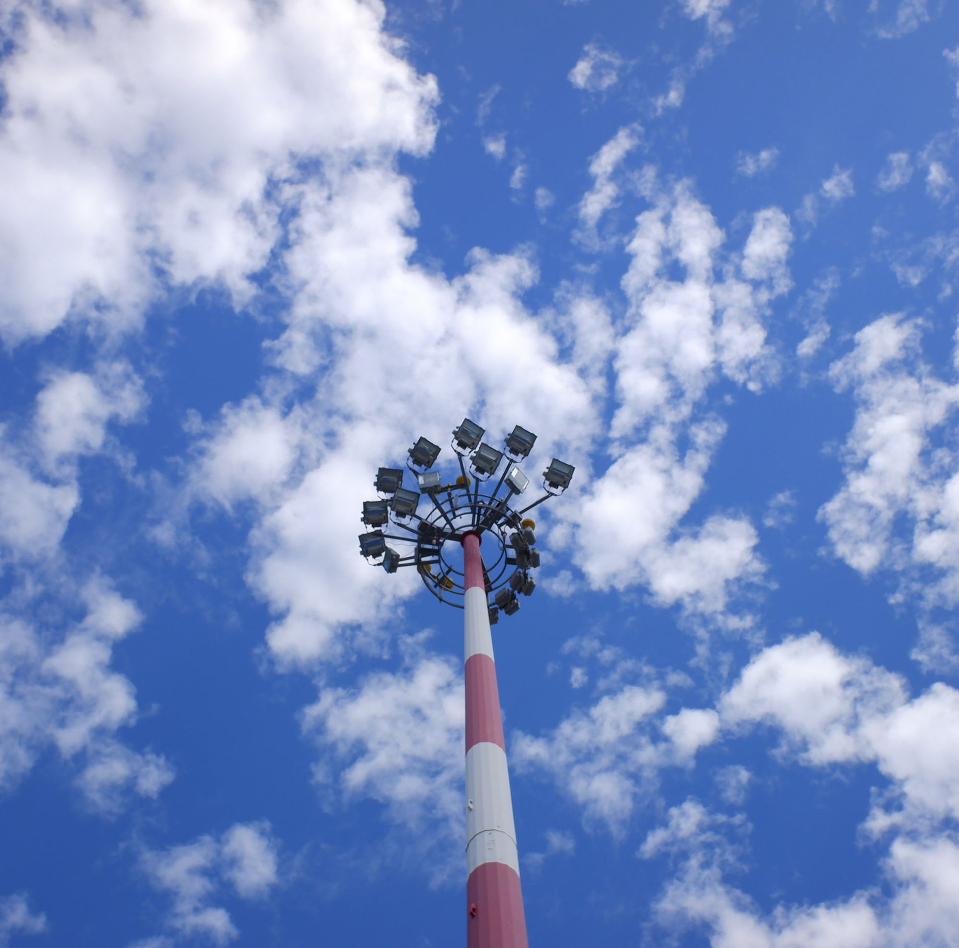 Tall red and white striped light tower against a bright blue sky with scattered white clouds.