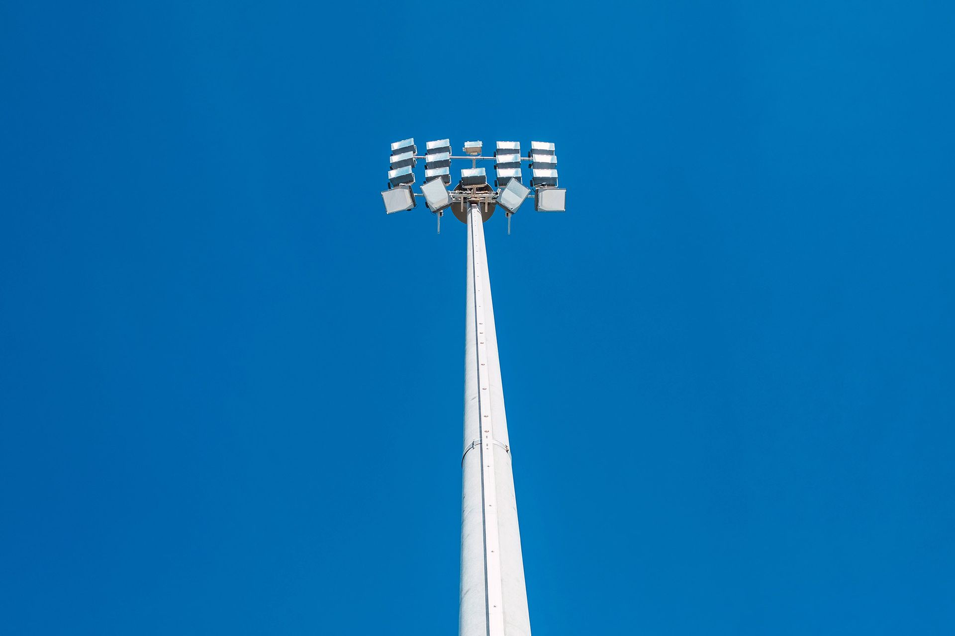White sports stadium light tower against a bright blue sky.