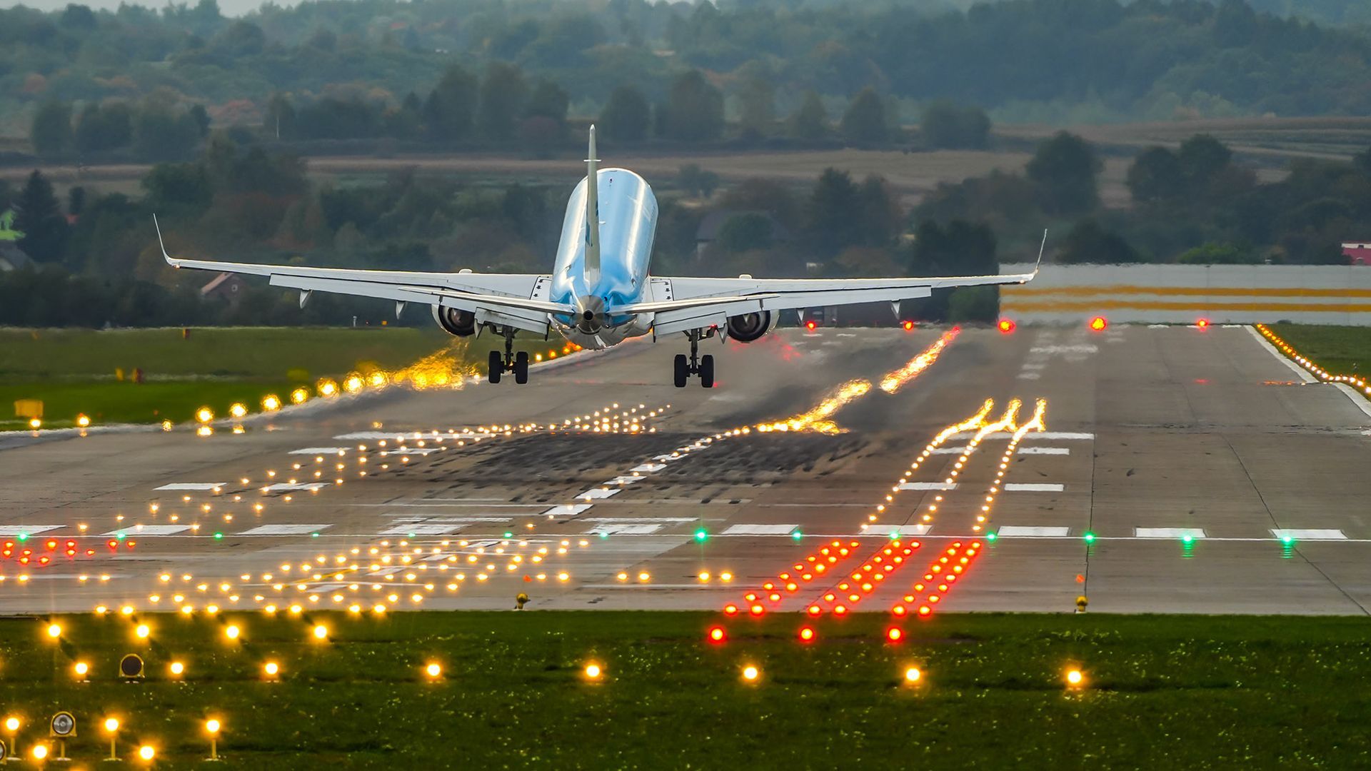 Airplane landing on illuminated runway at dusk.