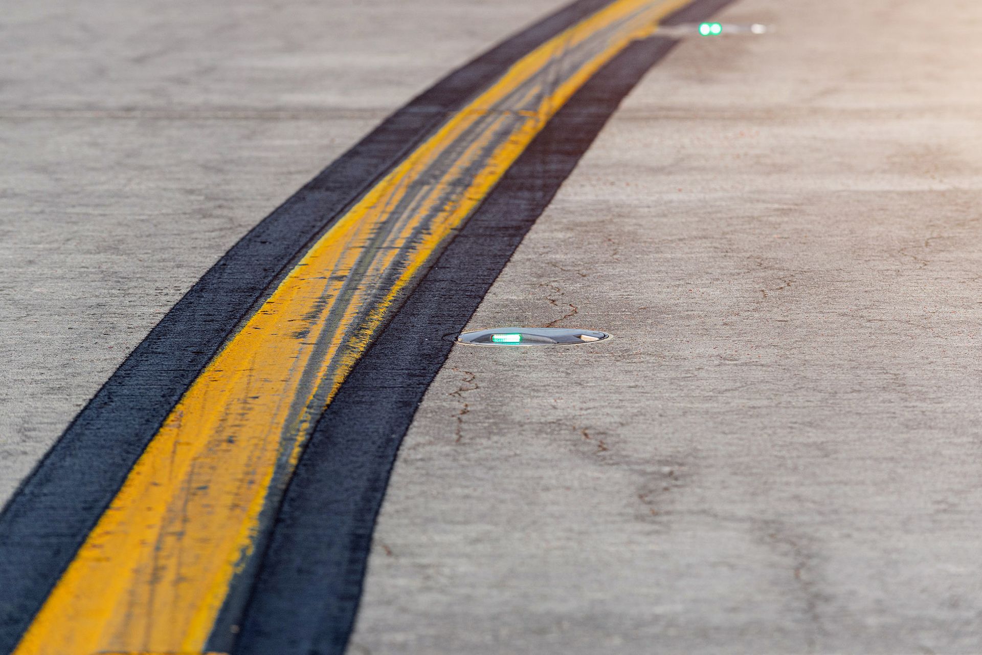 Yellow and black curved runway markings with embedded green lights on concrete surface.