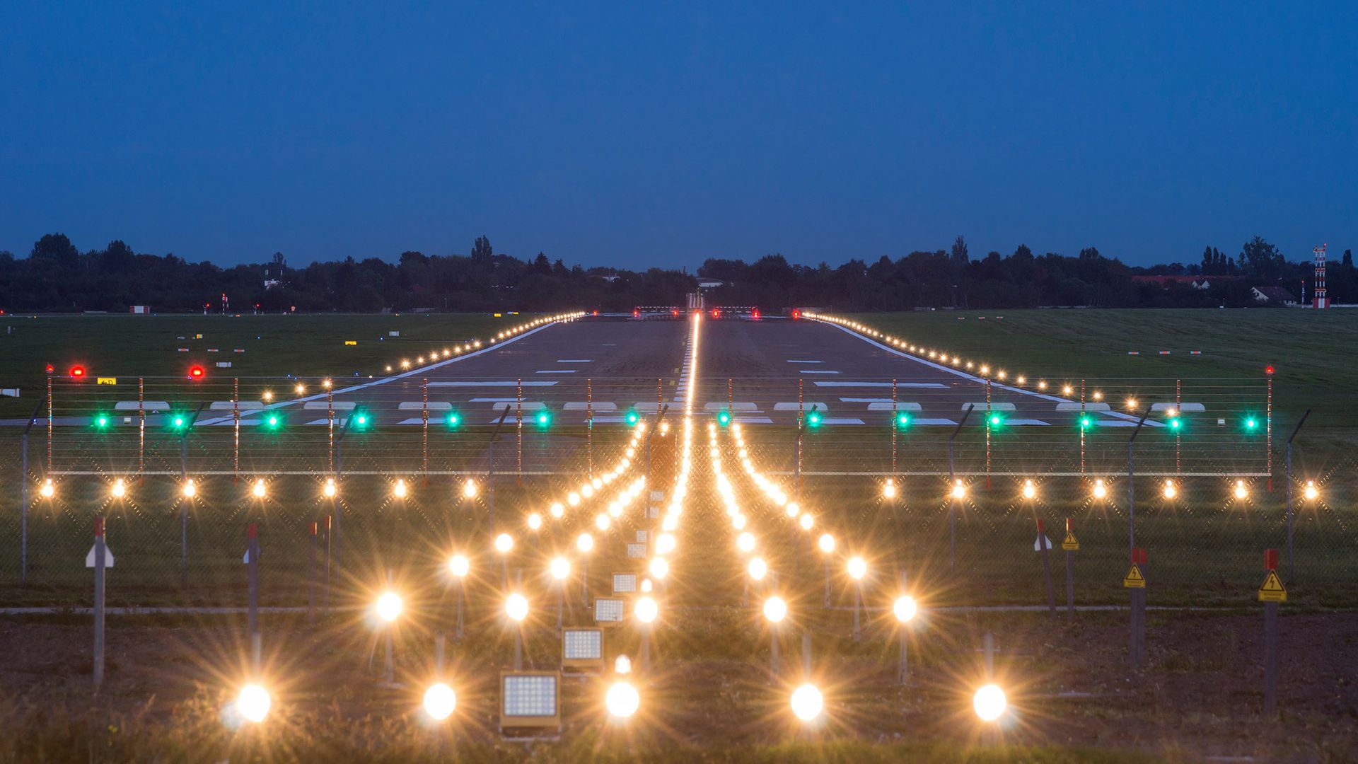 Lit airport runway at dusk, with bright lights leading to the horizon.