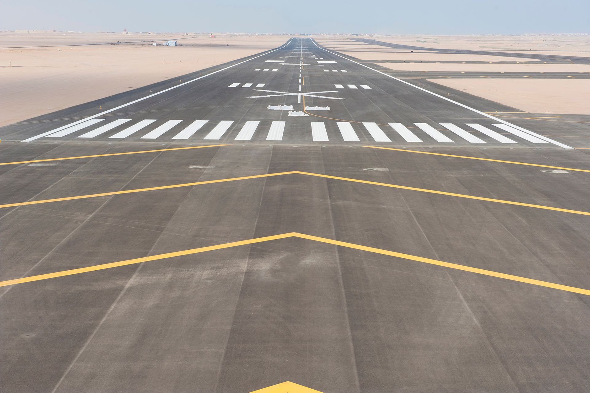 Airport runway with markings, extending into a desert landscape under a clear sky.