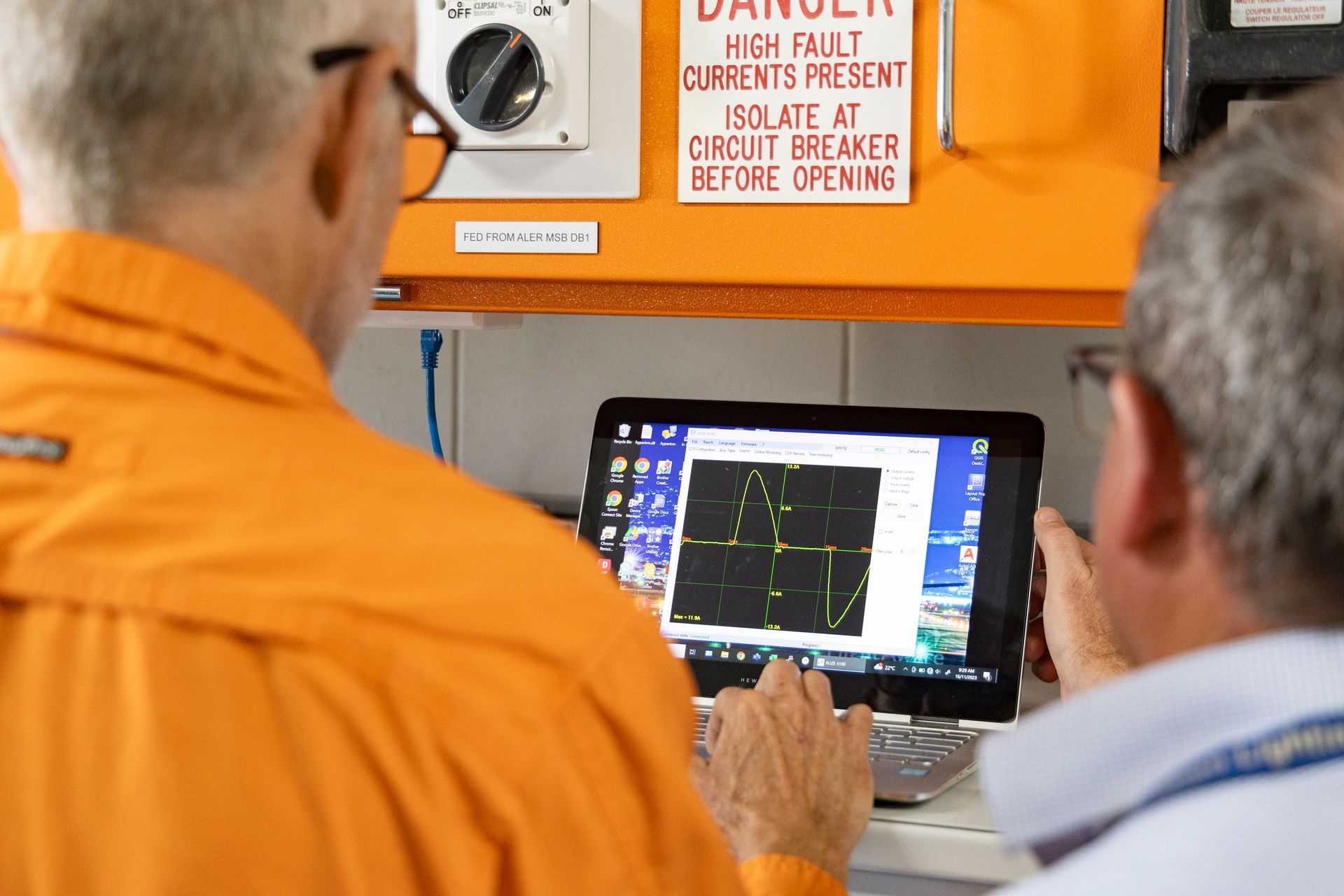 Person in safety vest, inspecting control panel, taking notes on clipboard.