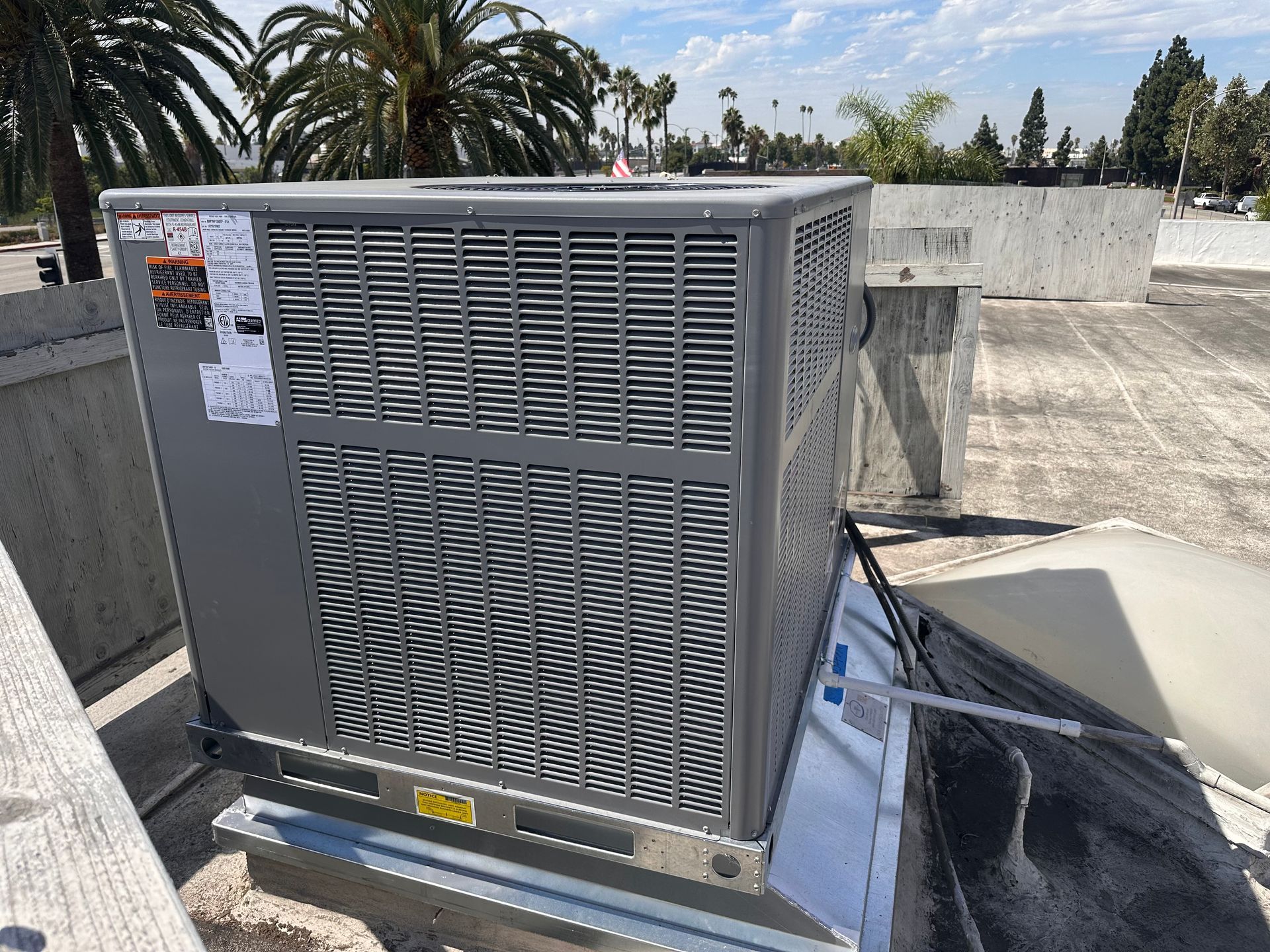 Gray air conditioning unit on a rooftop with palm trees in the background.