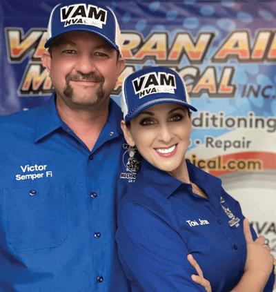 Two people in matching blue shirts and hats in front of a sign; one man and one woman smiling.