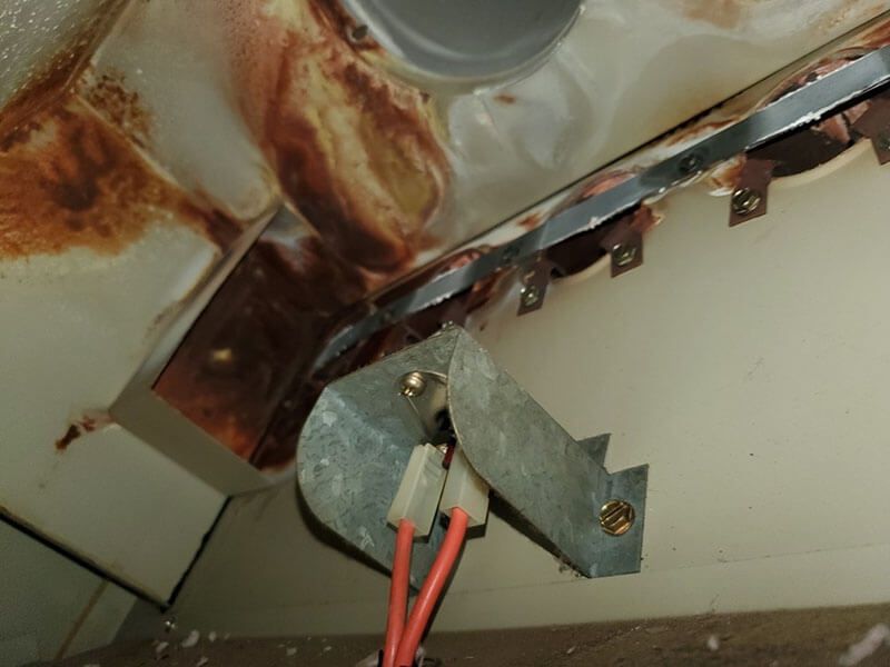 Inside a dirty appliance, possibly an oven, with brown stains and exposed electrical components.