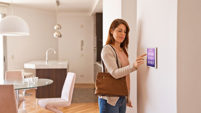 Woman using smart home control panel on a wall in a modern kitchen.