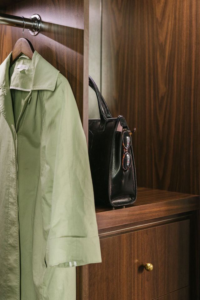 Two white suitcases with brown trim and a trench coat on a bed in a room.