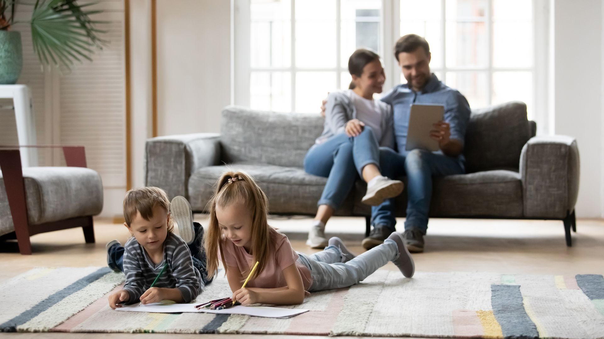 A family is sitting on a couch in a living room and drawing on the floor.