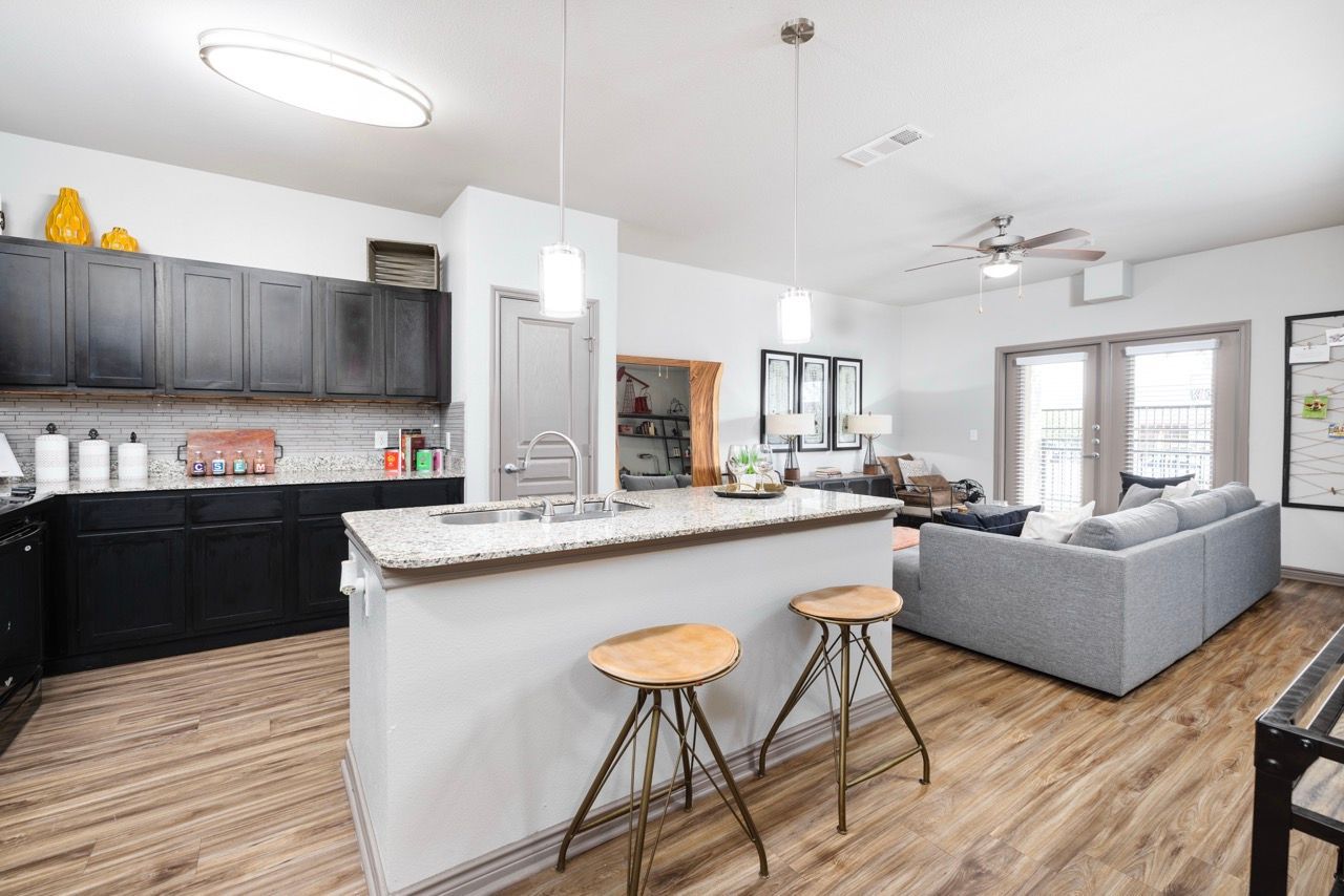 Open-concept kitchen with granite island, pendant lights, and a gray sectional living area.