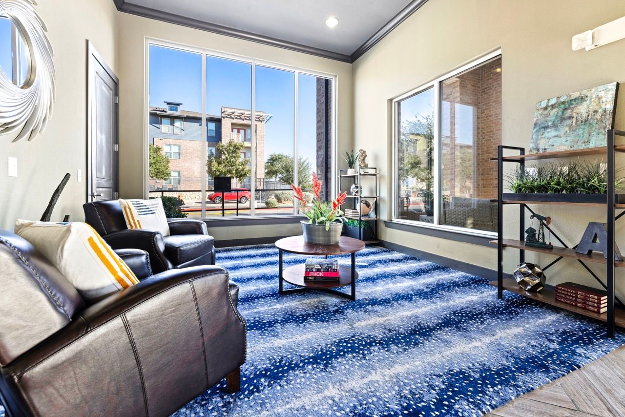 Bright common room with large windows, blue patterned rug, leather chairs, and shelving.