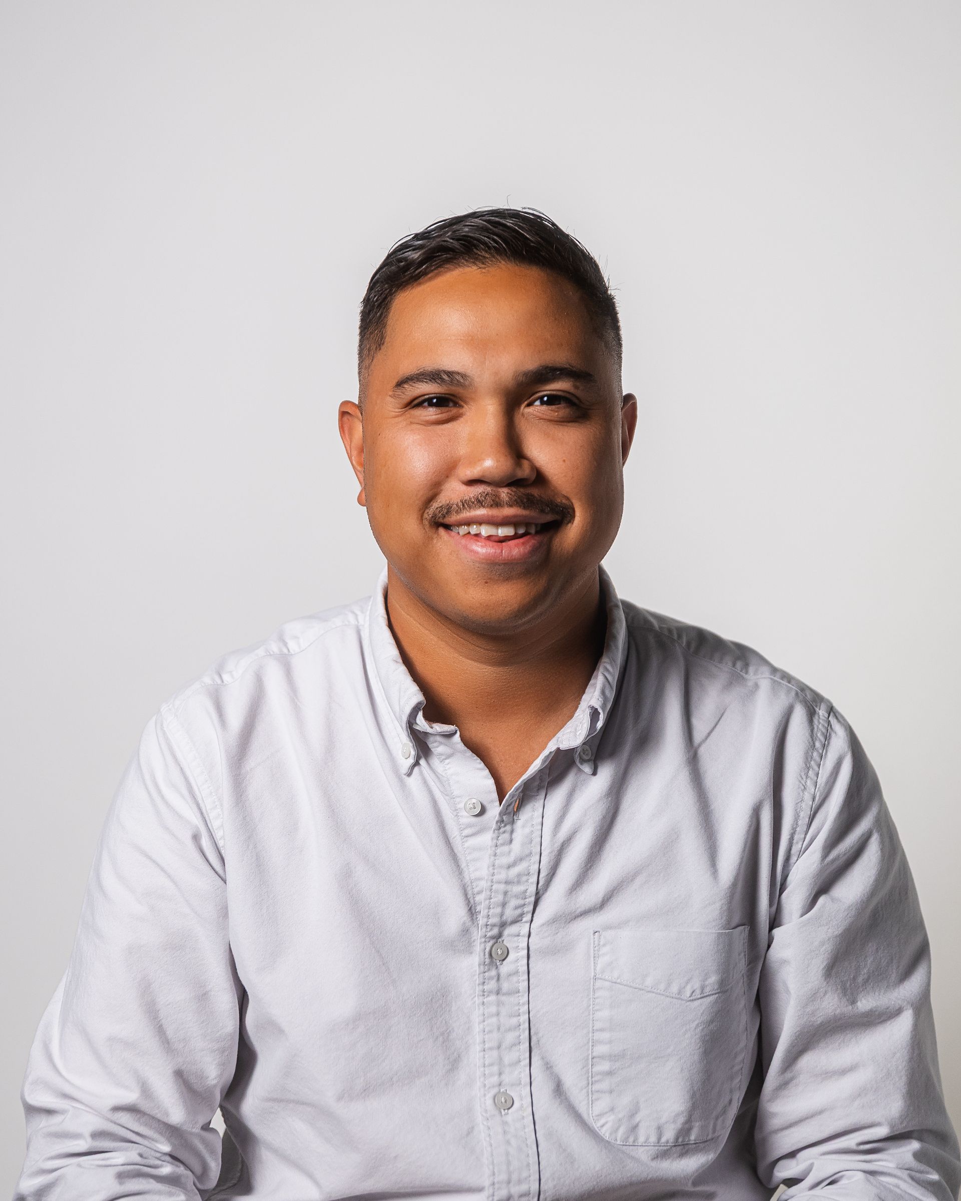 Homme souriant en chemise claire boutonnée sur fond blanc.