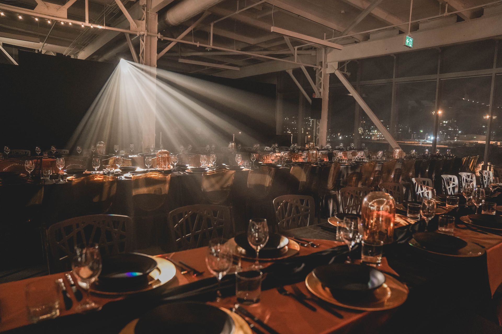 Dîner formel, tables dressées, éclairées par un projecteur, vue de la ville en arrière-plan.