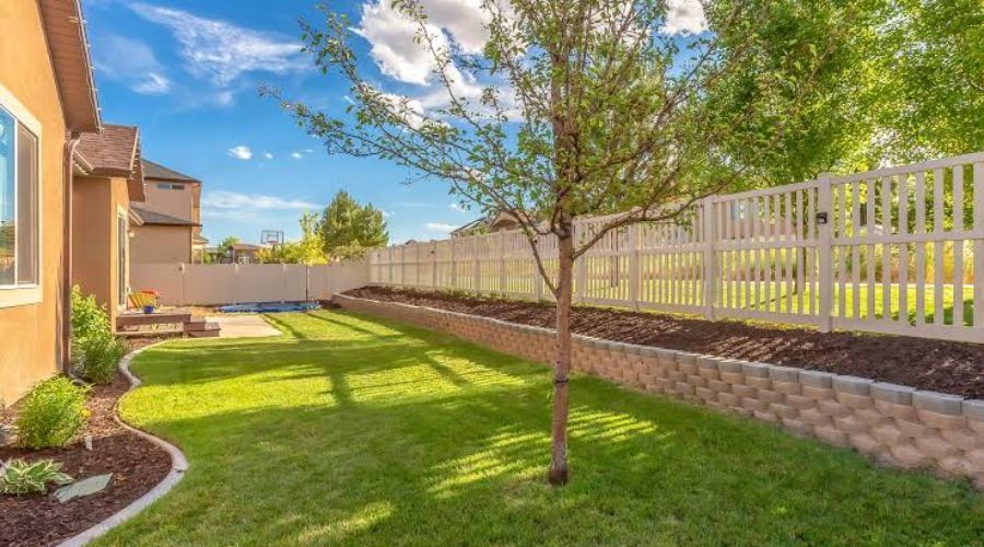 White vinyl fence installed on a stone retaining wall in a backyard.