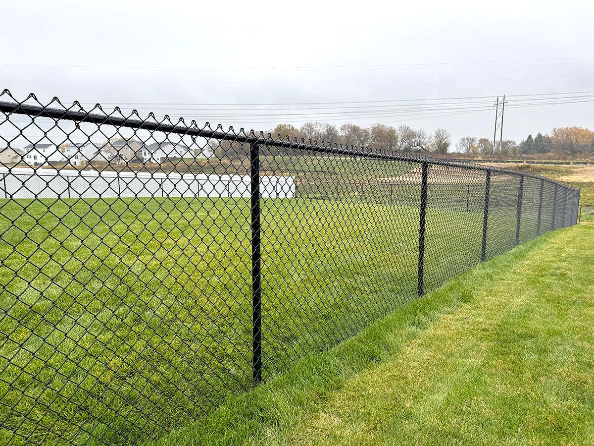 A black chain-link fence runs along a green grass field under a cloudy sky.