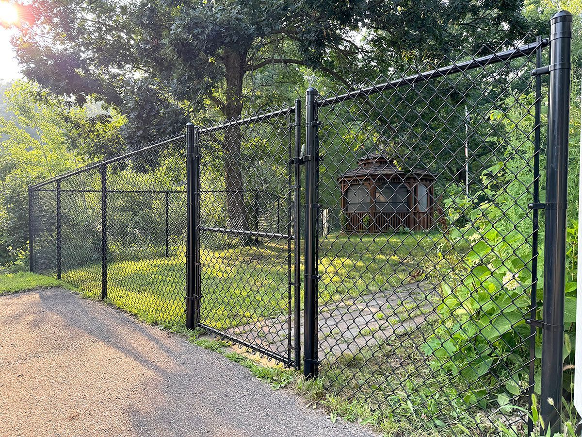 A black chain-link fence with a closed gate bordering a grassy area containing a gazebo and trees.