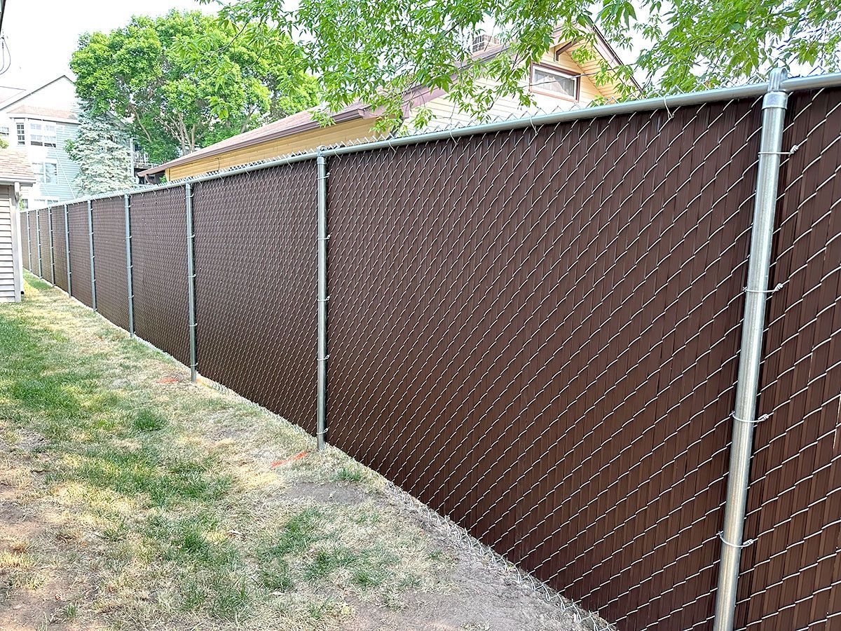 A dark brown privacy fence made of chain-link with vertical plastic slats installed in a residential backyard.