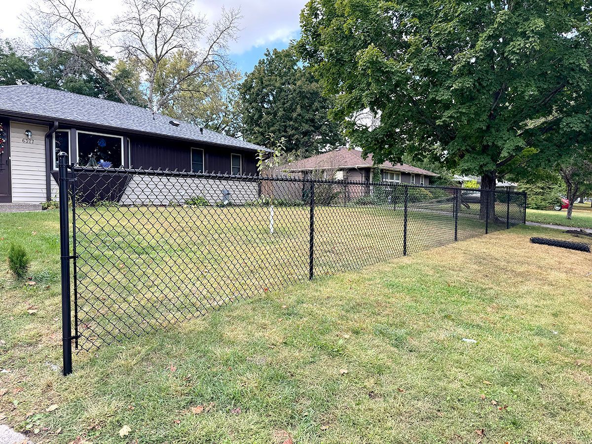 A black chain-link fence spans a grassy front yard in front of a house on a suburban street.