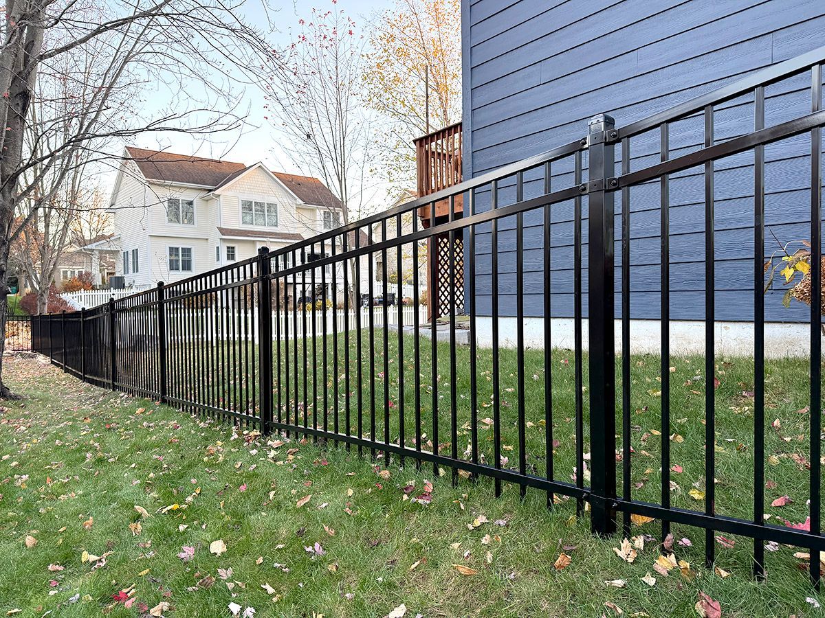Black metal fence segments following a downward slope on a lawn next to a blue house.