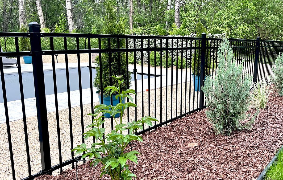 A black metal fence surrounds a backyard pool area with landscaping, including shrubs and dark mulch.