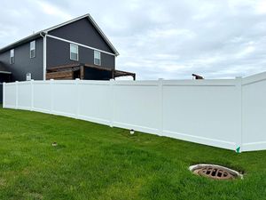 A white vinyl privacy fence stands in a green grassy yard in front of a dark-sided two-story house.