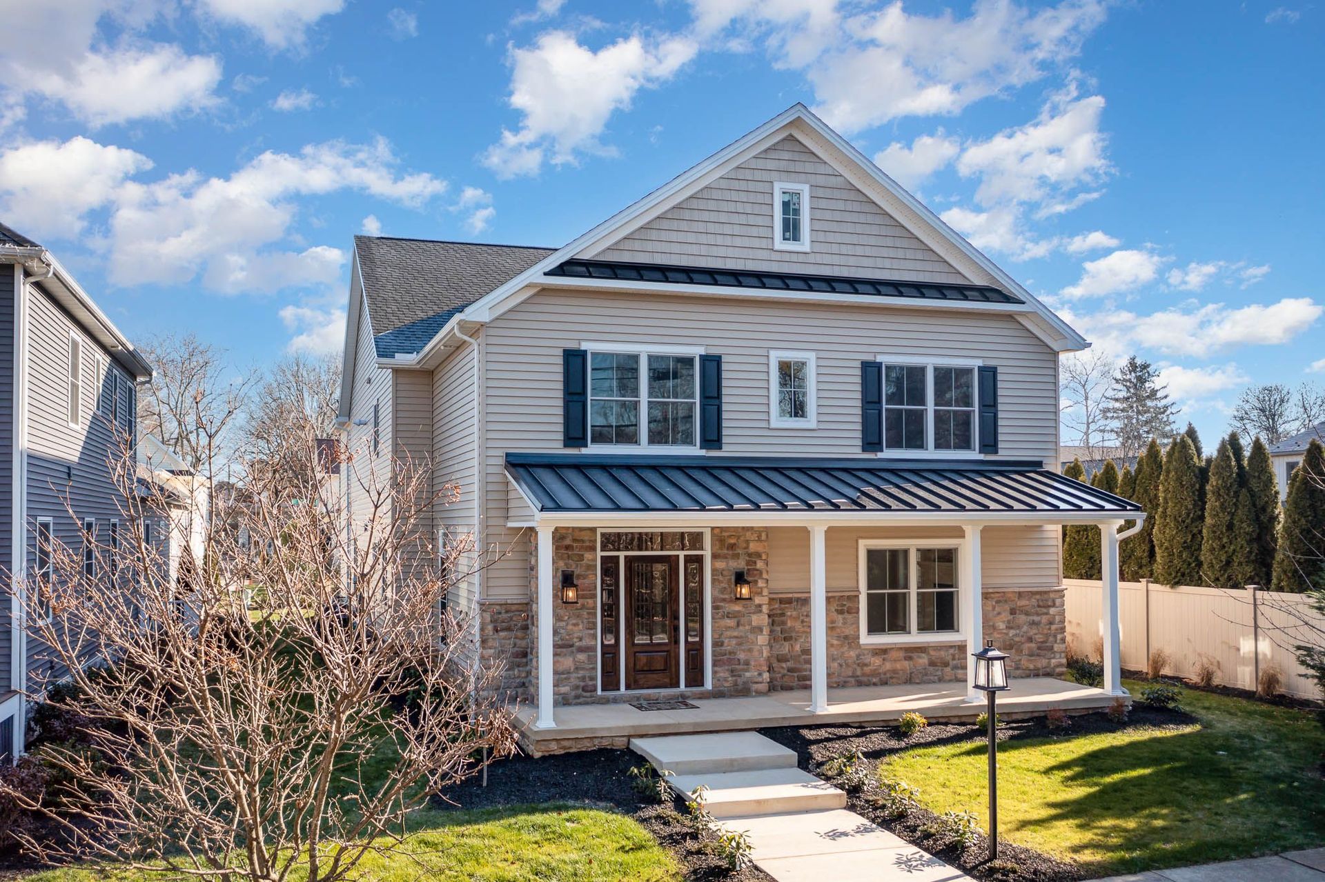 Two-story house with light siding and stone accents, blue shutters, and a covered porch.