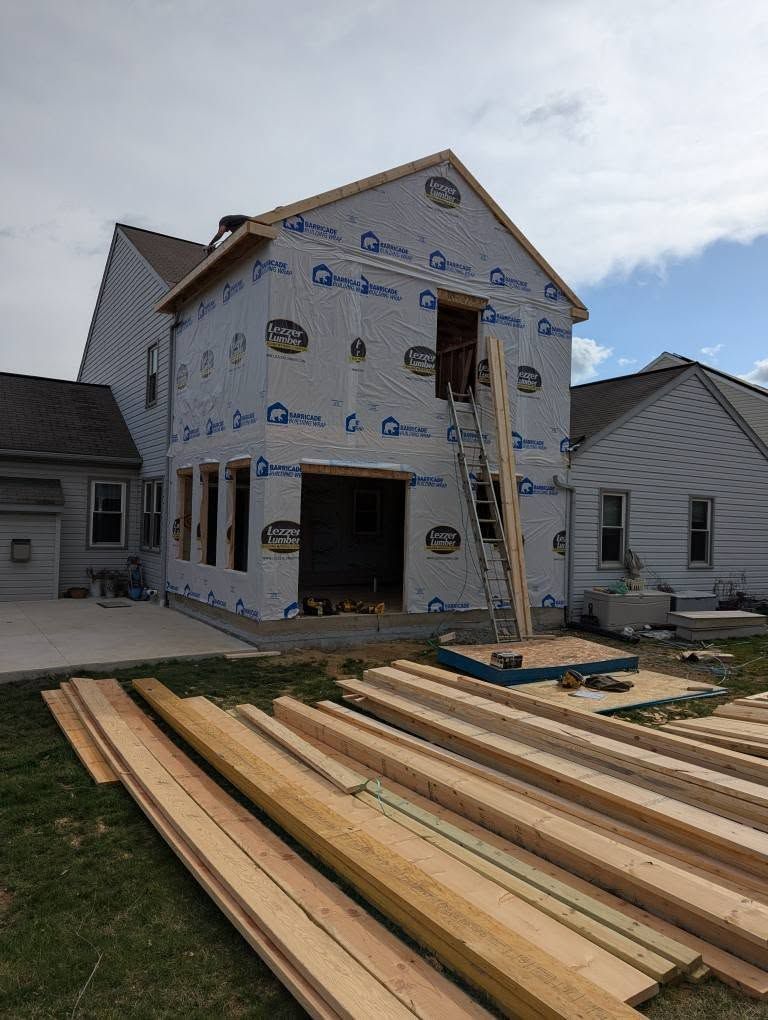 Construction in progress on a two-story house addition, with lumber in the foreground.