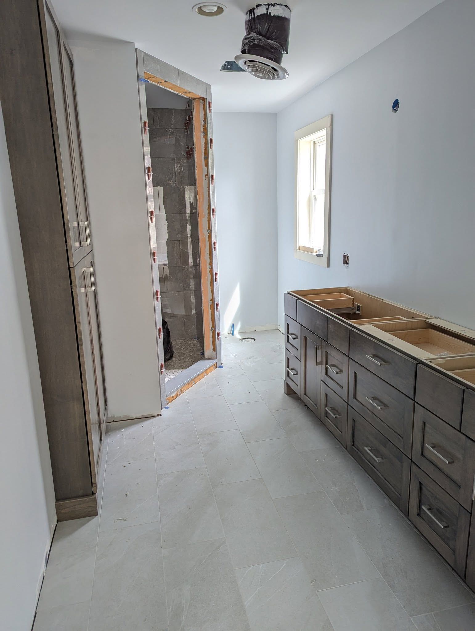 Bathroom under construction, with gray cabinets, shower entrance, and light walls.