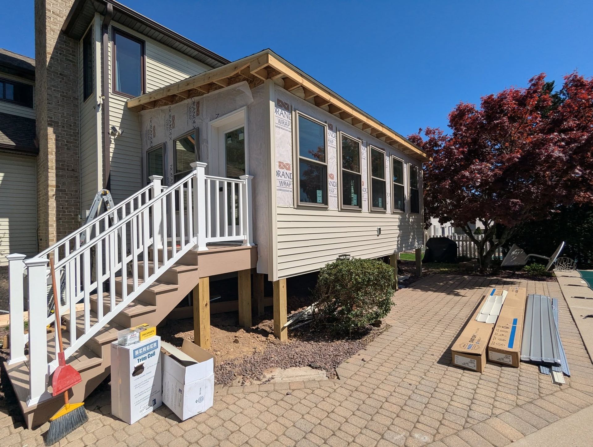 Sunroom addition on deck. Building exterior, new windows, and materials on patio. Sunny day.
