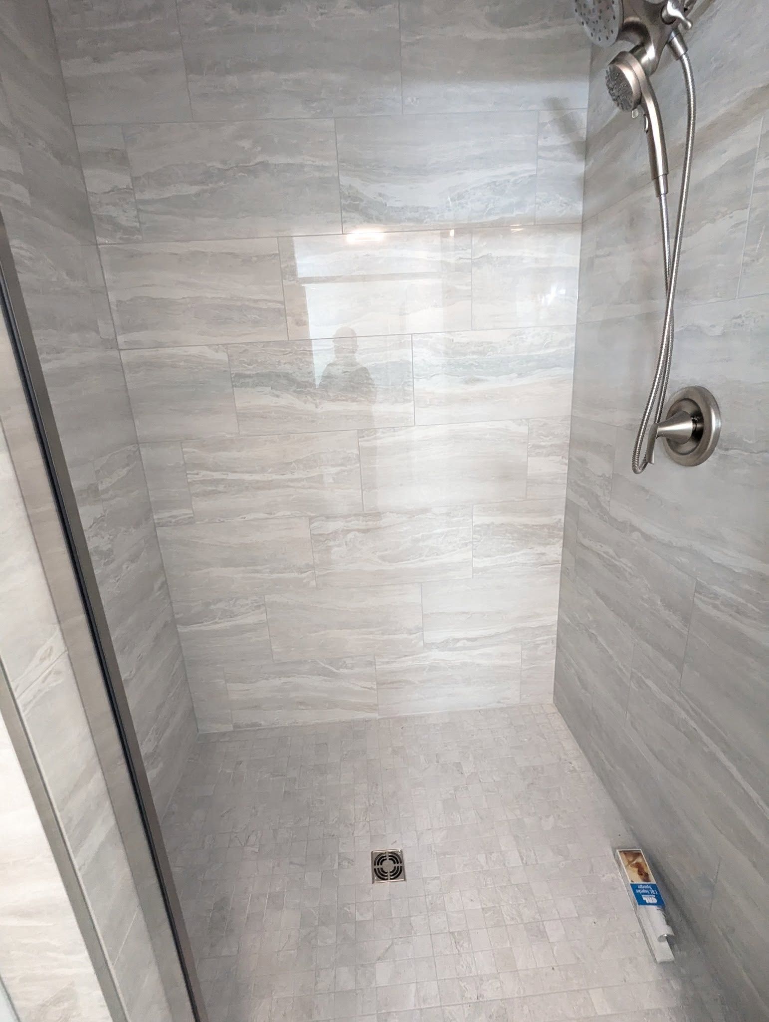 Shower with light gray tile walls and floor, glass enclosure, and silver shower fixtures.