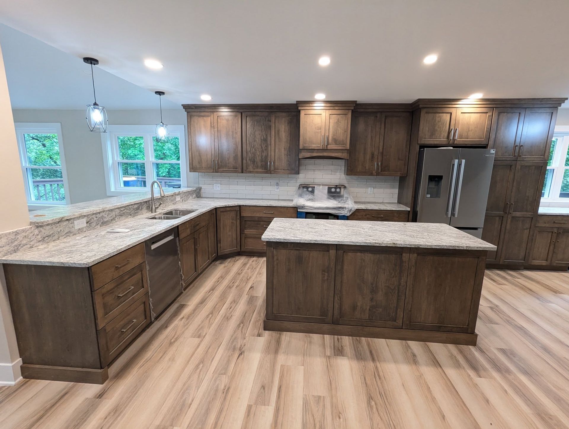 Kitchen with wood cabinets, island, granite countertops, stainless steel appliances, and light wood flooring.