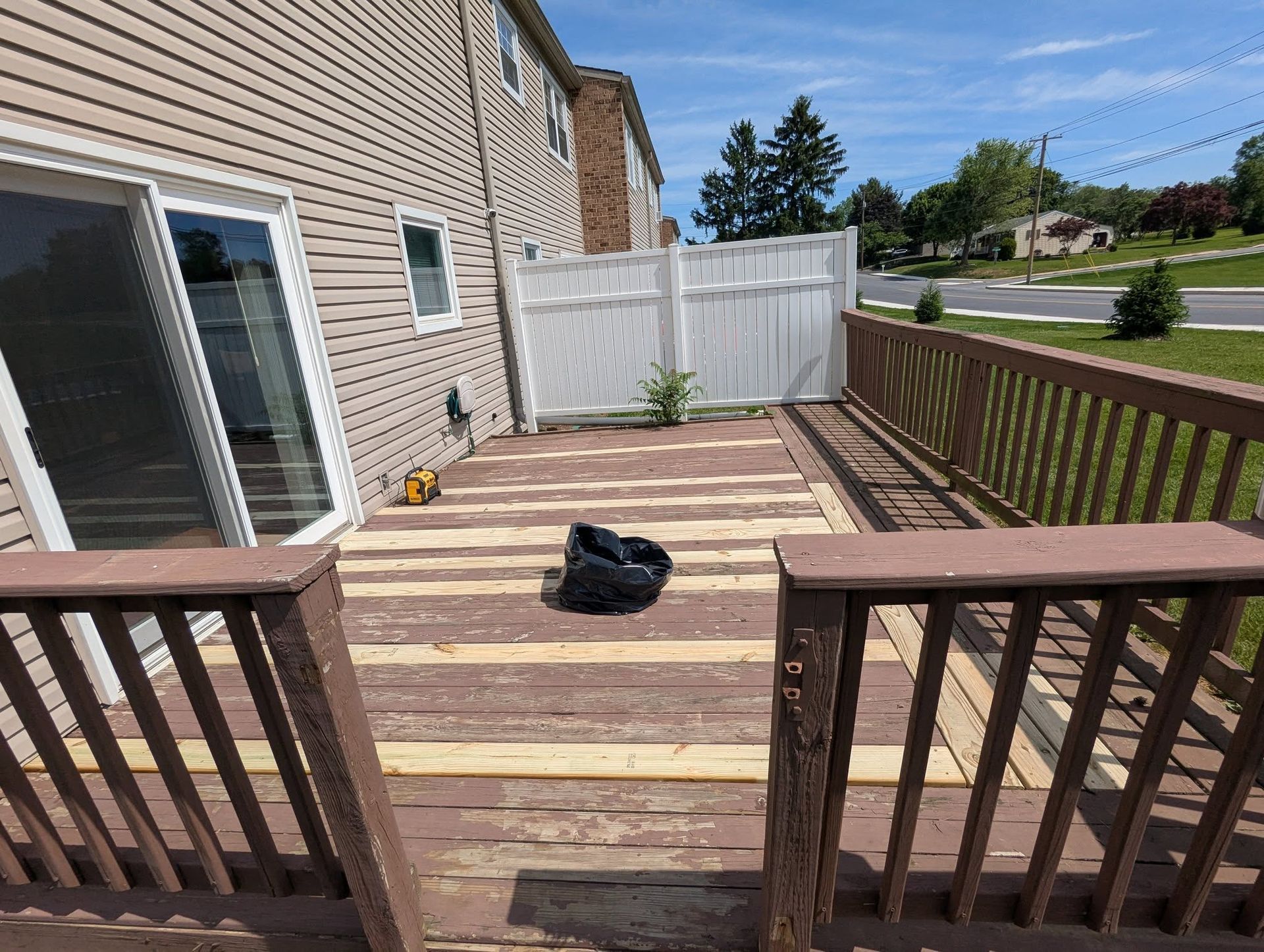 Deck with weathered wooden planks, brown railing, white fence, and sliding glass door. Overcast sky.