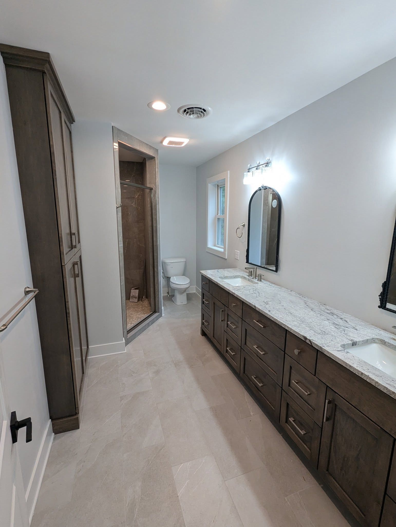 Bathroom with long vanity, granite countertop, tall cabinet, and shower.
