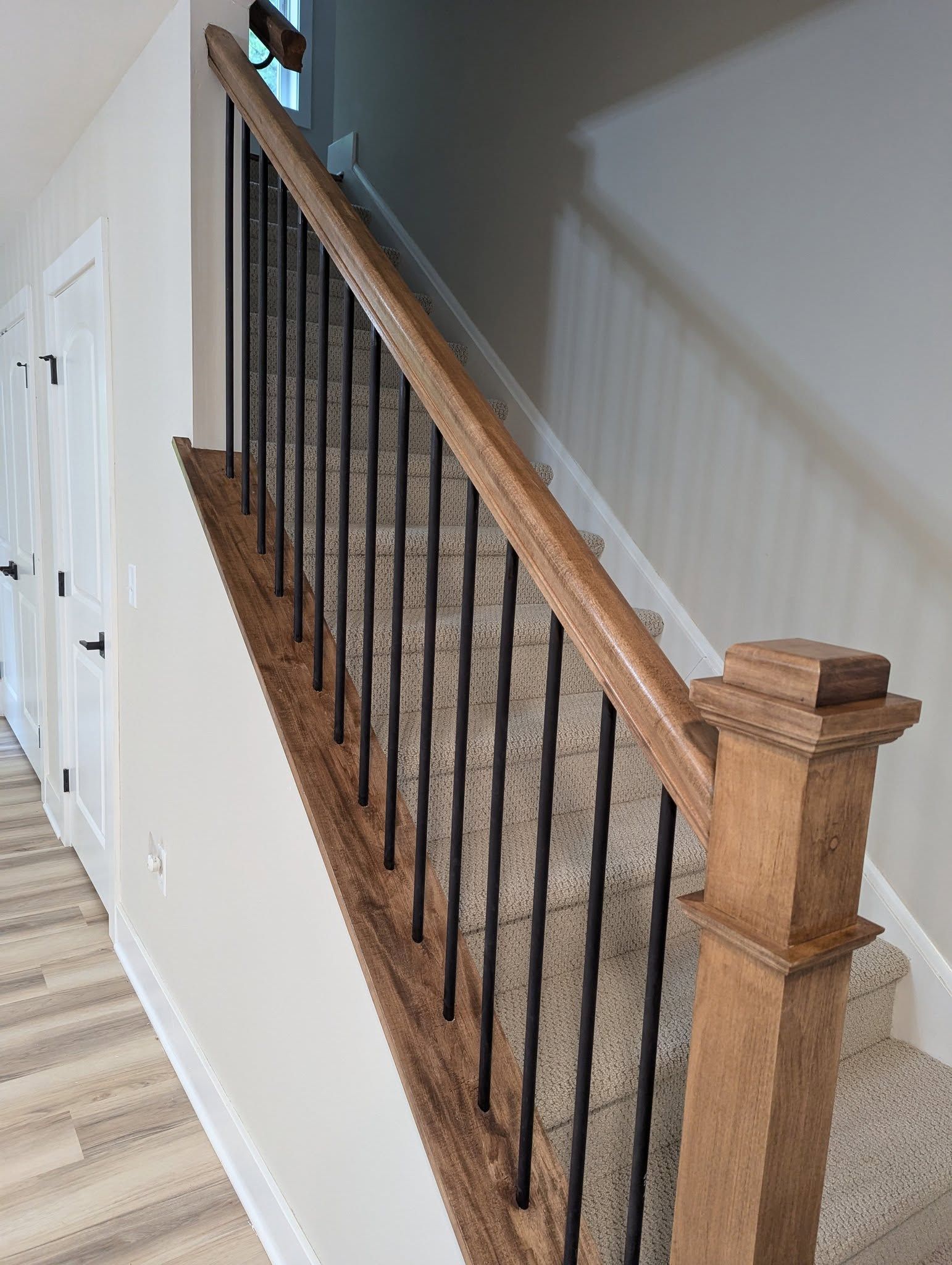 Staircase with wooden handrail, black spindles, and carpeted steps.