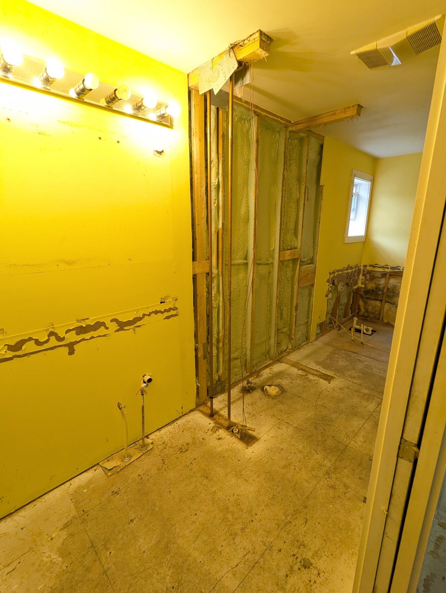 Bathroom under renovation with yellow walls, exposed studs, and rough concrete floor.