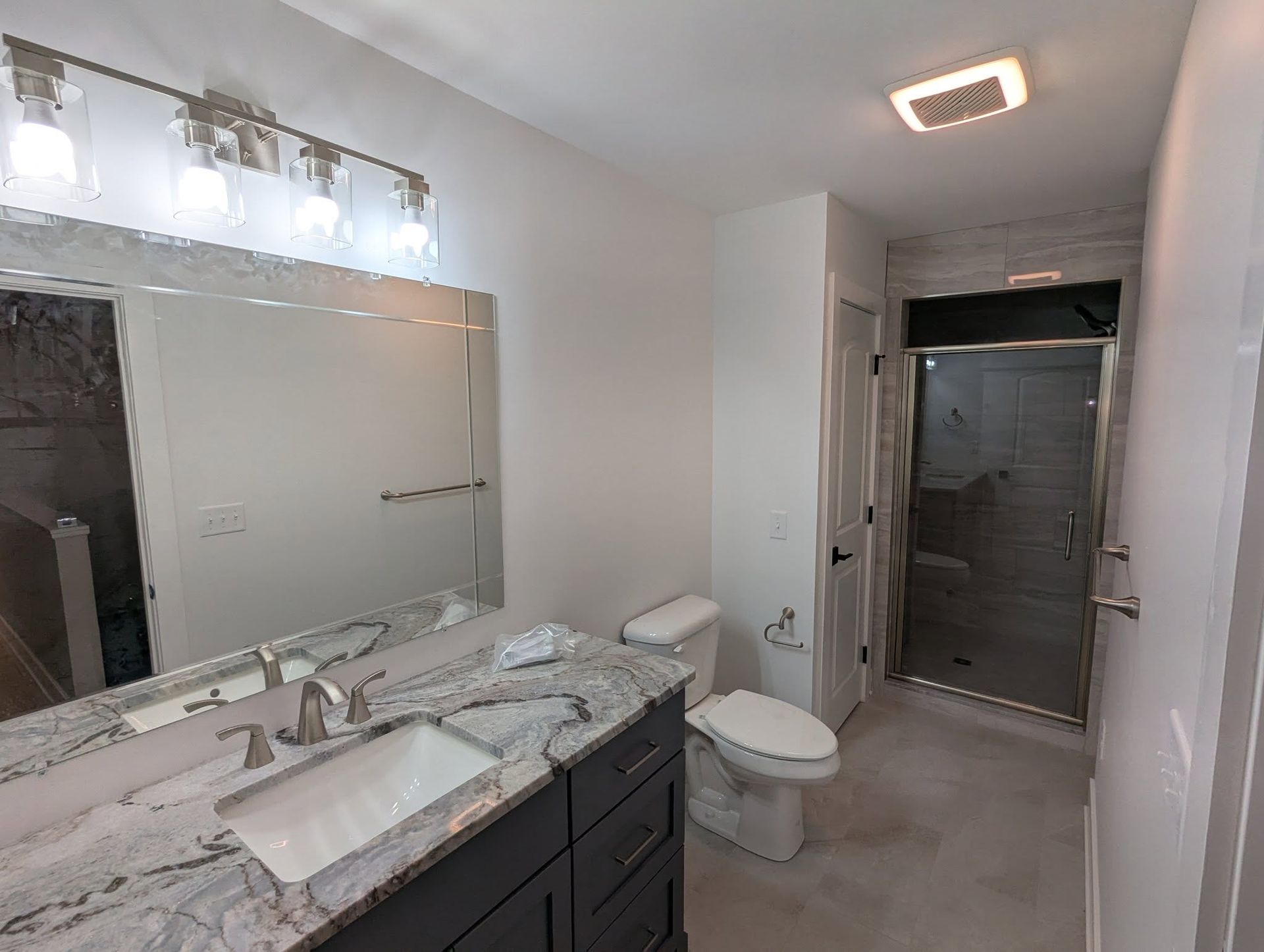 Bathroom with gray vanity, white toilet, glass shower, and rectangular mirror.