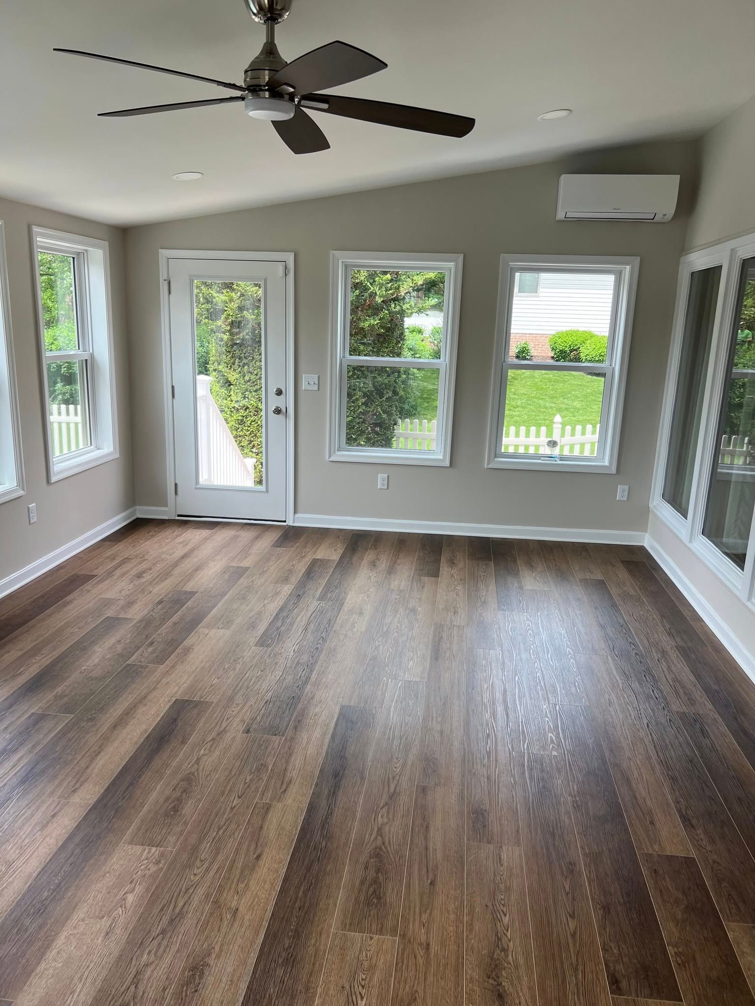 Sunroom with wood-look floor, windows, door to a deck, and a ceiling fan.