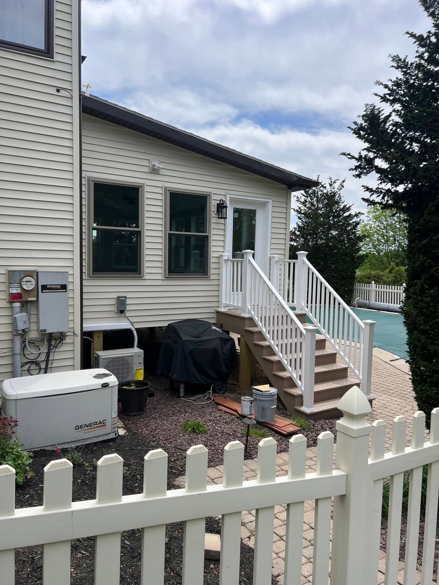 Exterior view of a house with a white fence, deck with stairs, two windows, and a door. Cloudy sky.